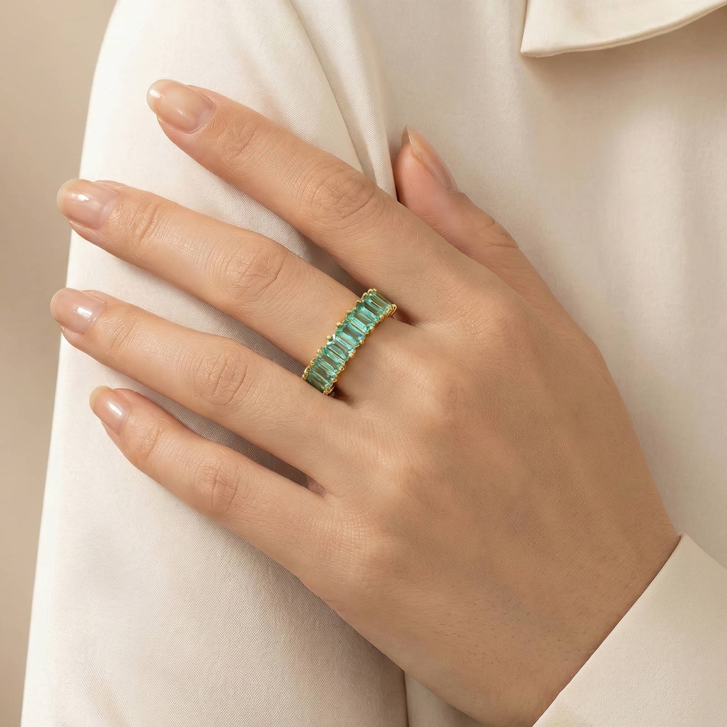 Hand wearing a green emerald ring on a beige background