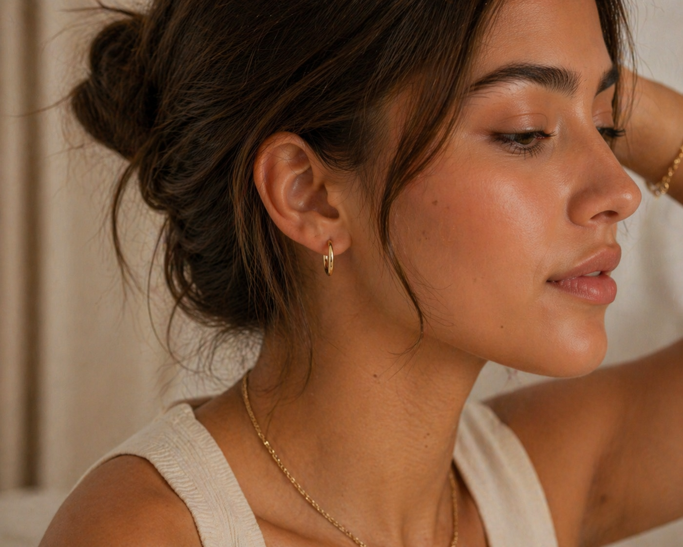 Close-up of a woman wearing gold earrings and a necklace with a neutral background