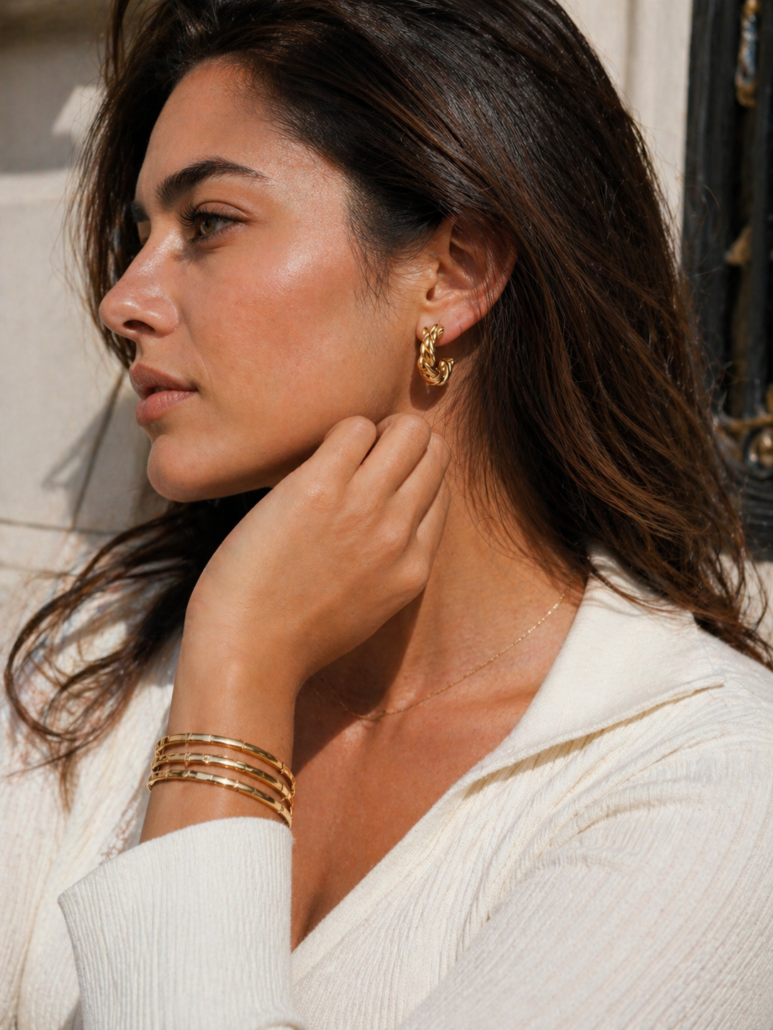 Woman wearing gold earrings and bracelets, with a neutral background