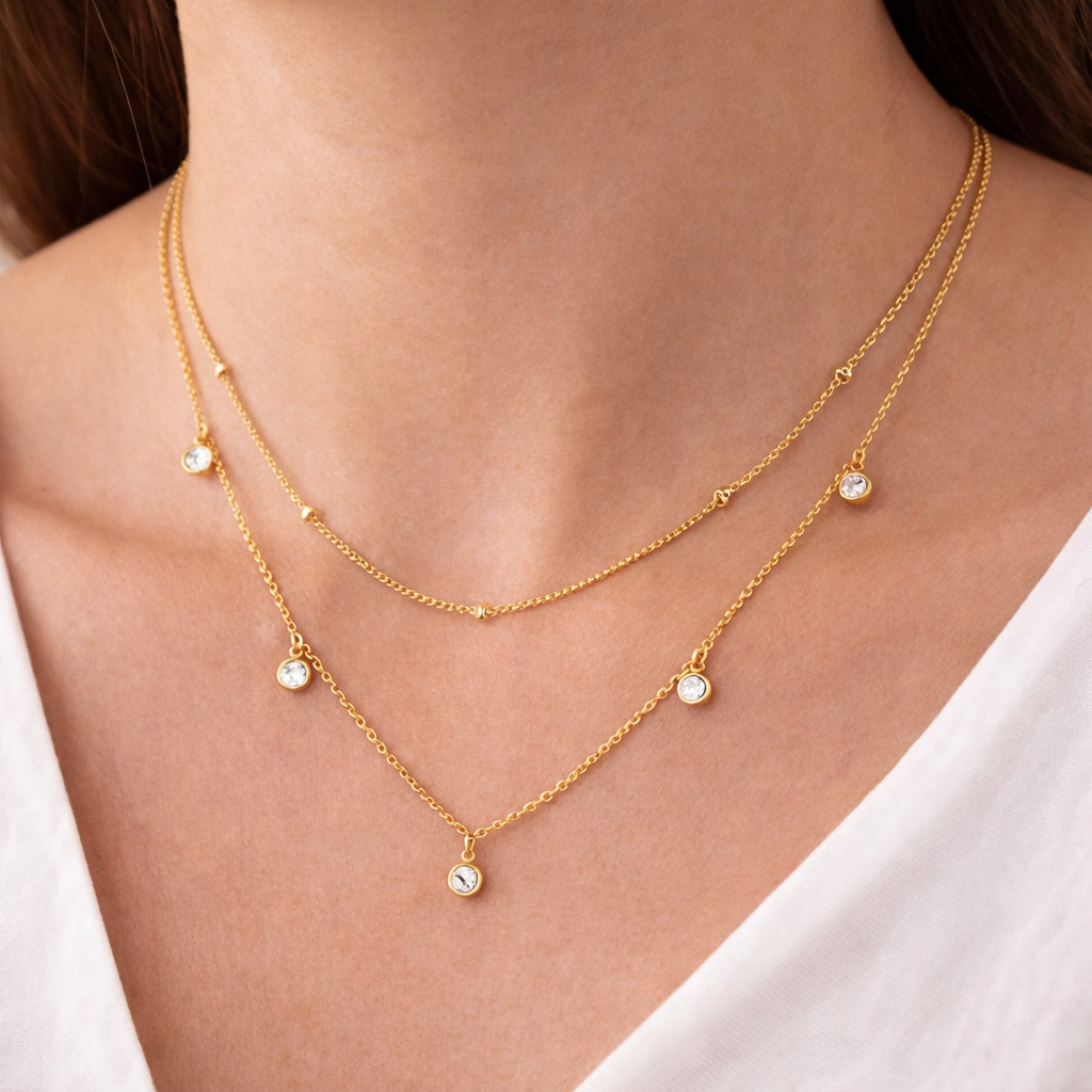 Gold necklace with small gemstones on a person wearing a white top.