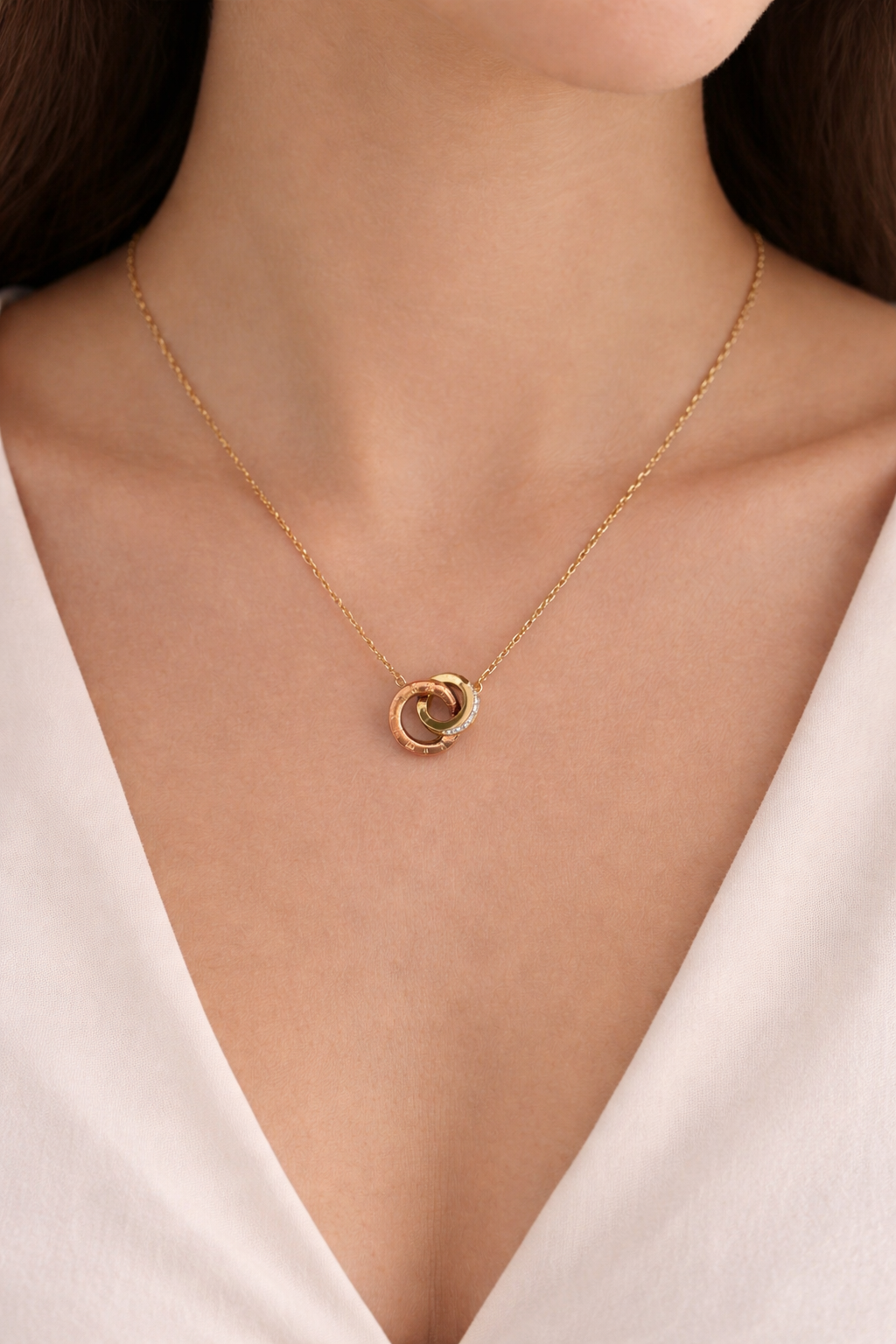 Gold necklace with a circular pendant on a person wearing a white top.