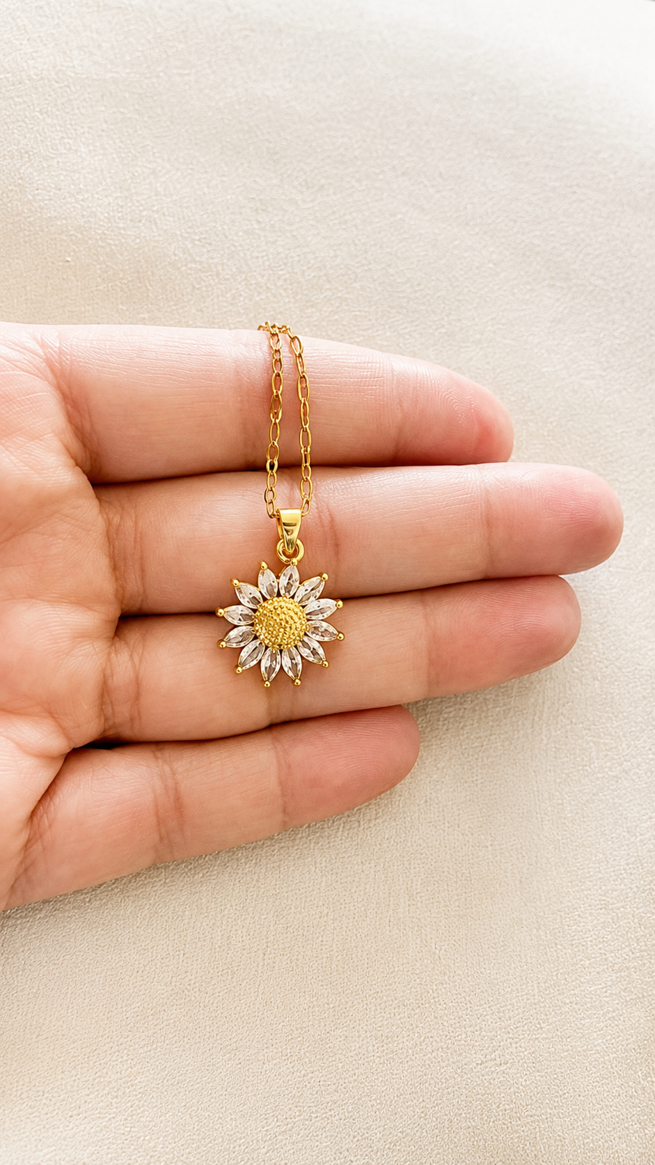 Gold necklace with a sunflower pendant held between fingers on a beige background
