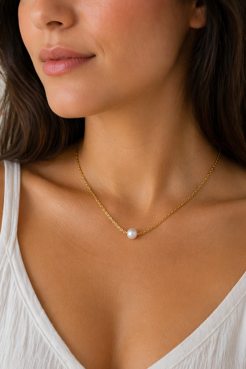 Woman wearing a gold necklace with a pearl pendant against a neutral background