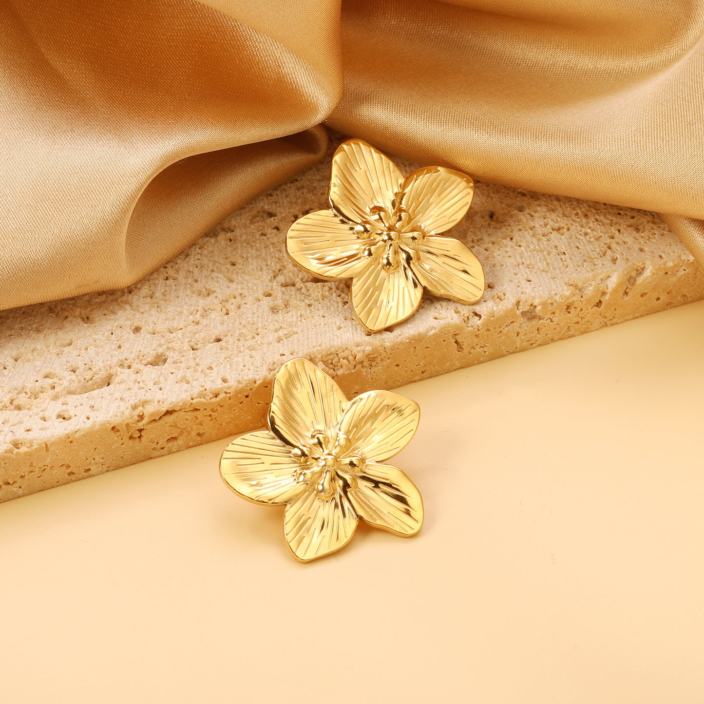 Gold flower-shaped earrings on a beige fabric background