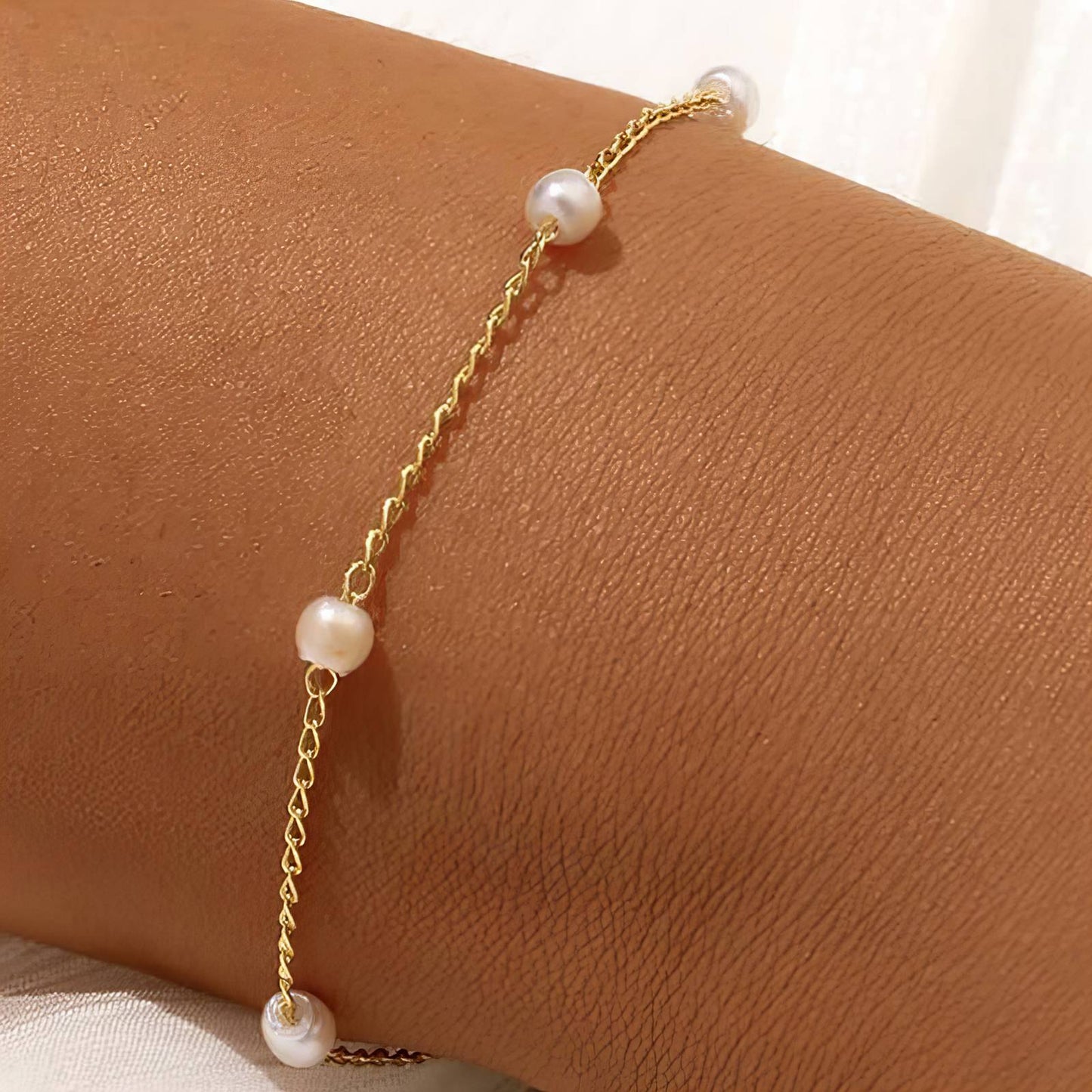 Gold bracelet with pearls on a wrist against a neutral background