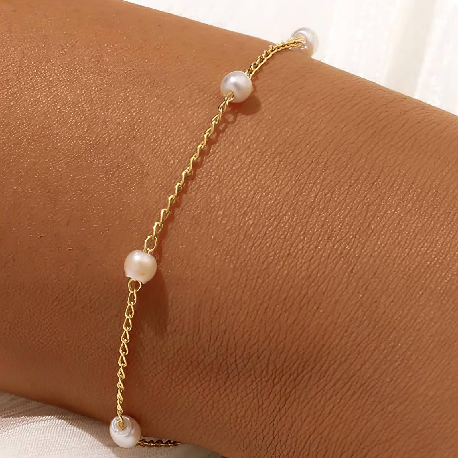 Gold bracelet with pearls on a wrist against a neutral background