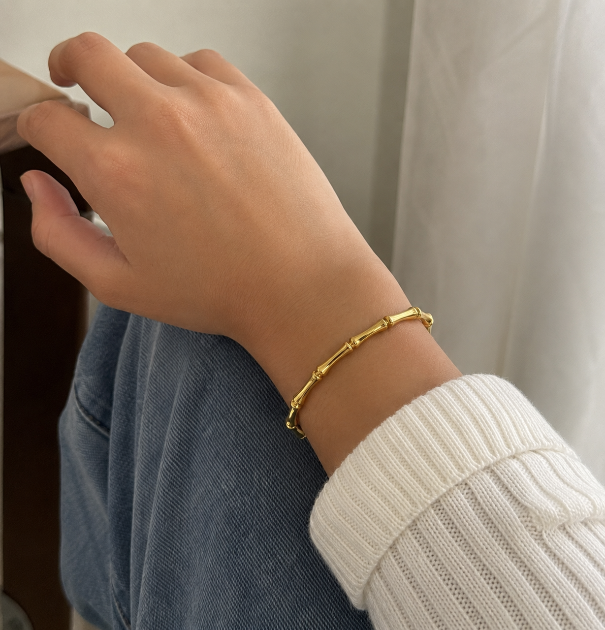 Hand wearing a gold bracelet with a neutral background