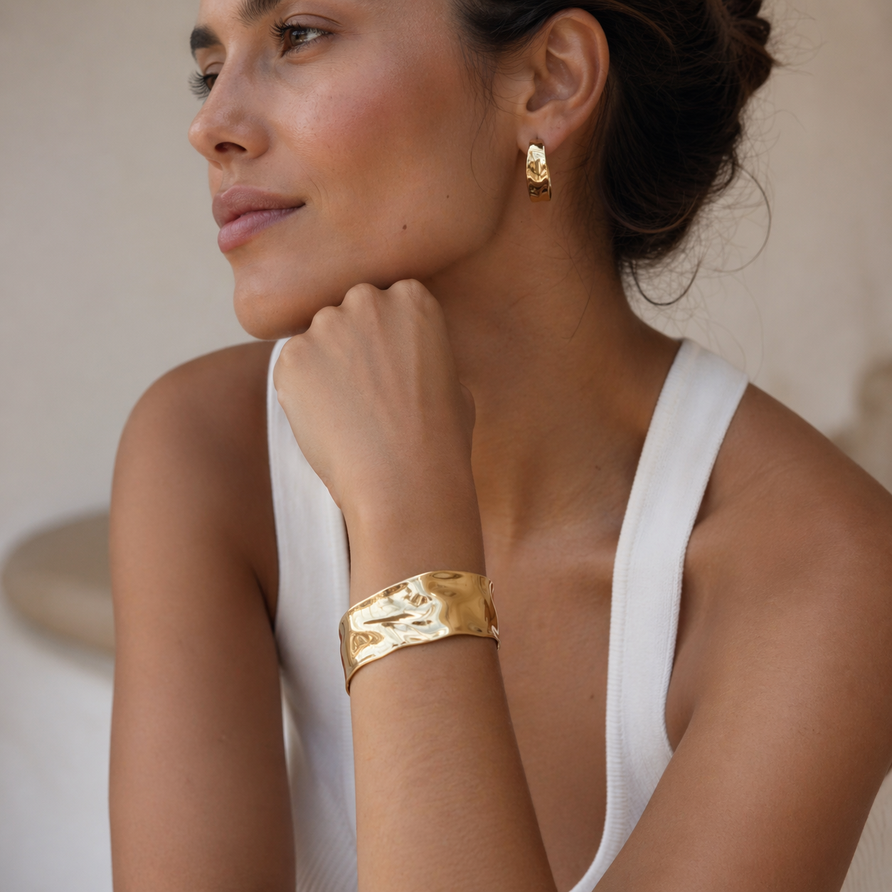 Woman wearing gold bracelet and earrings against a neutral background