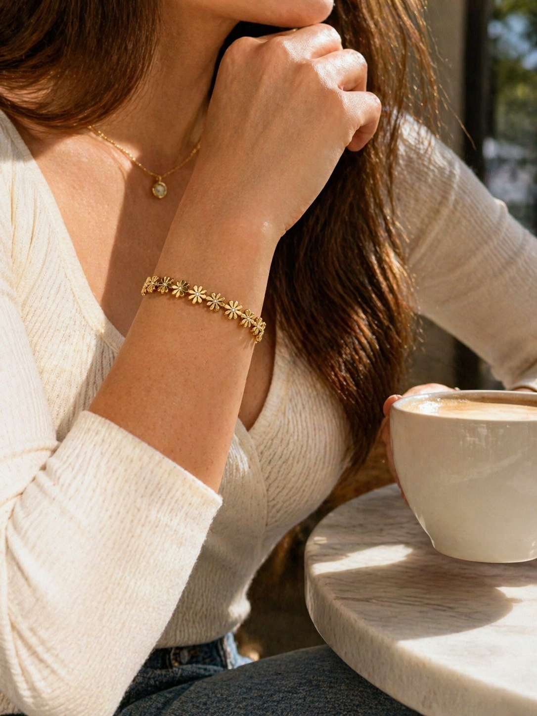 Person wearing a gold bracelet with star designs, holding a cup of coffee.