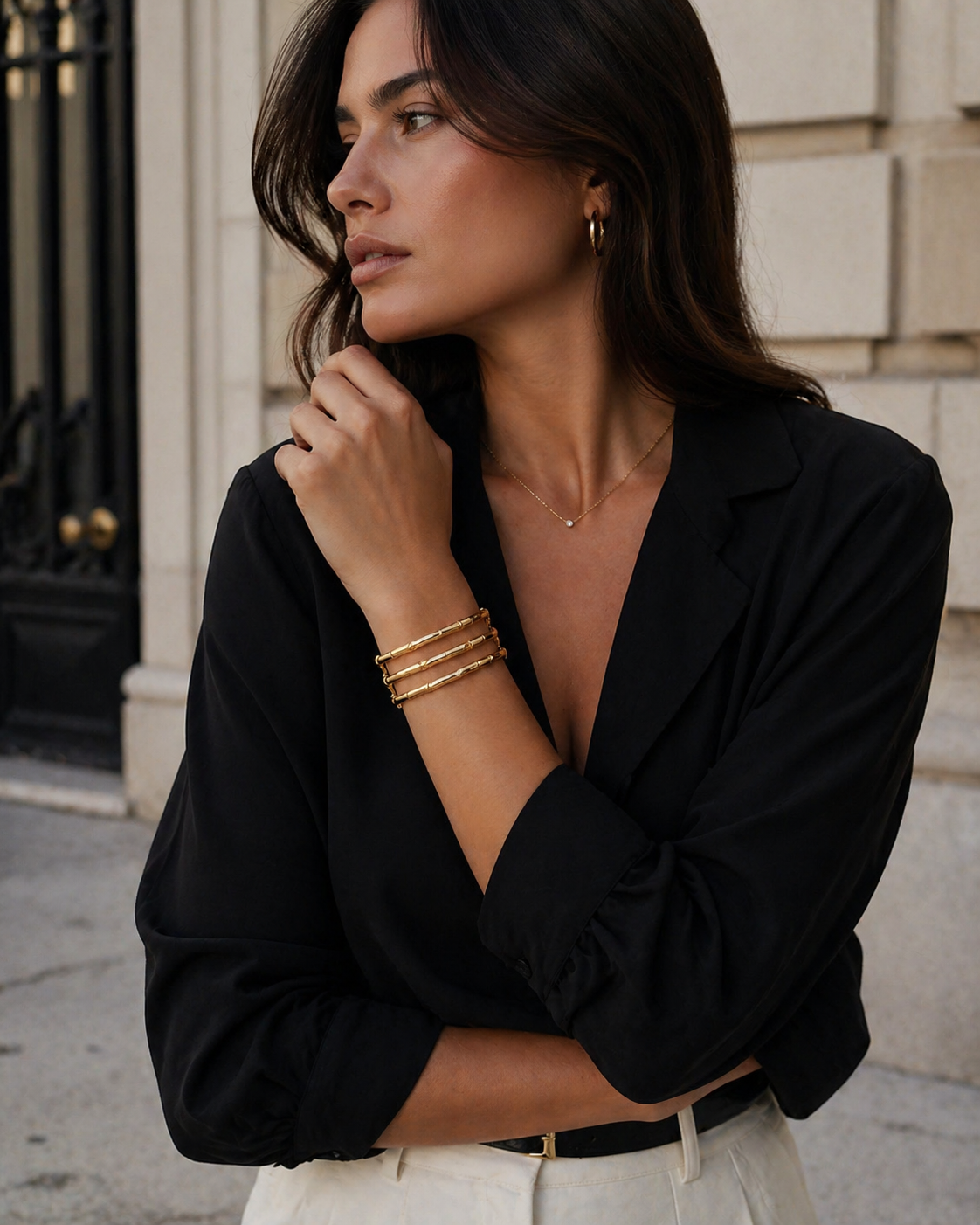 Woman wearing a black blouse with a deep neckline and gold jewelry outdoors.