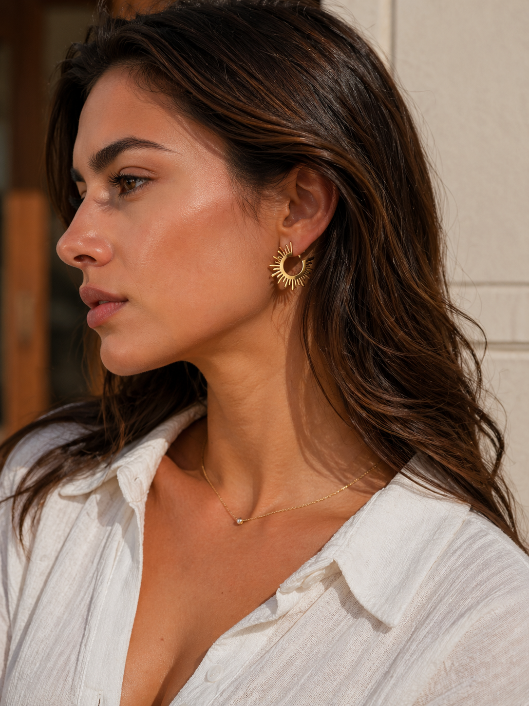 Woman wearing gold hoop earrings and a necklace, with a neutral background