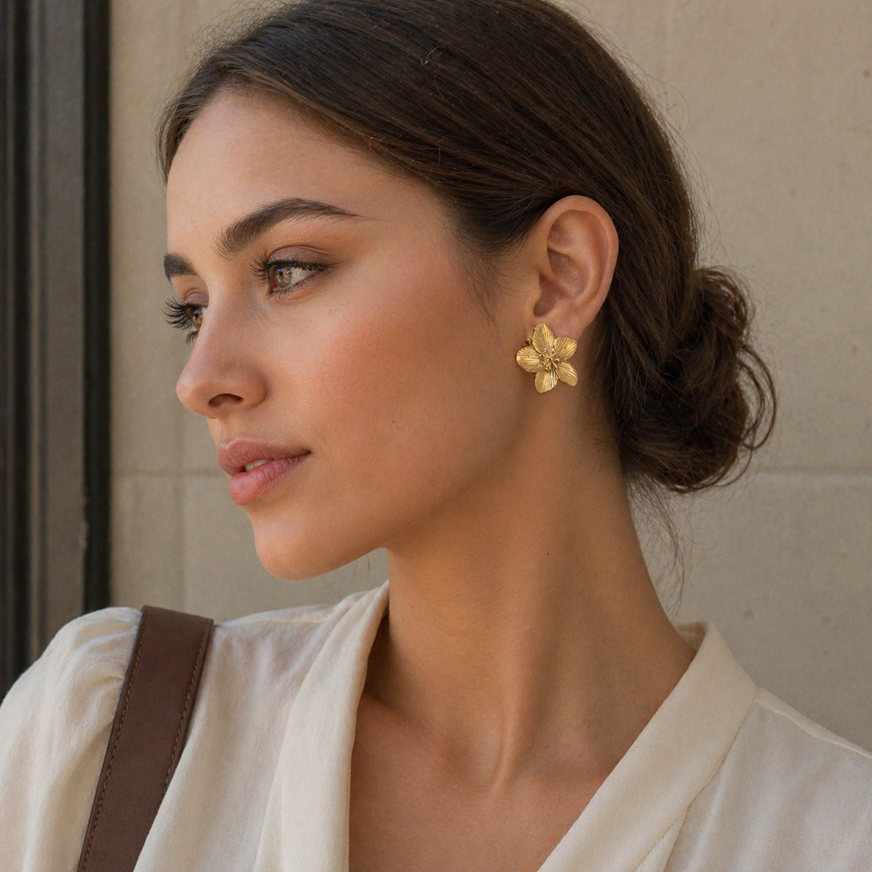 Woman wearing gold floral earrings with a neutral background