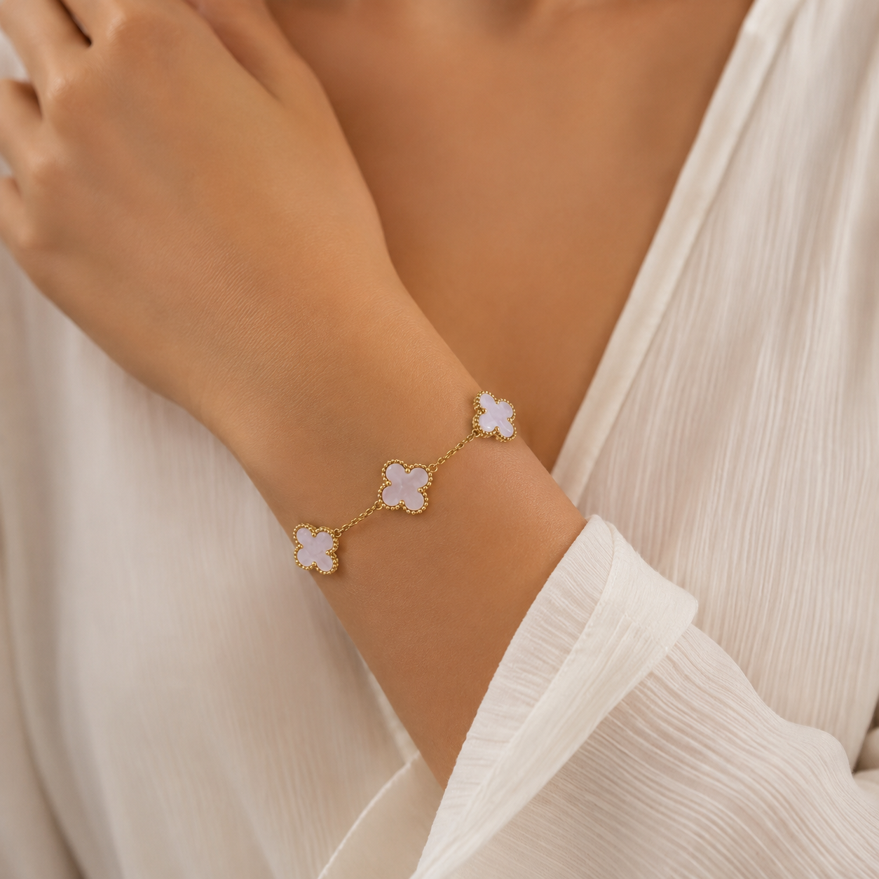 A delicate gold chain bracelet with three small four-petal flower charms in pale pink enamel, worn on a model's wrist.