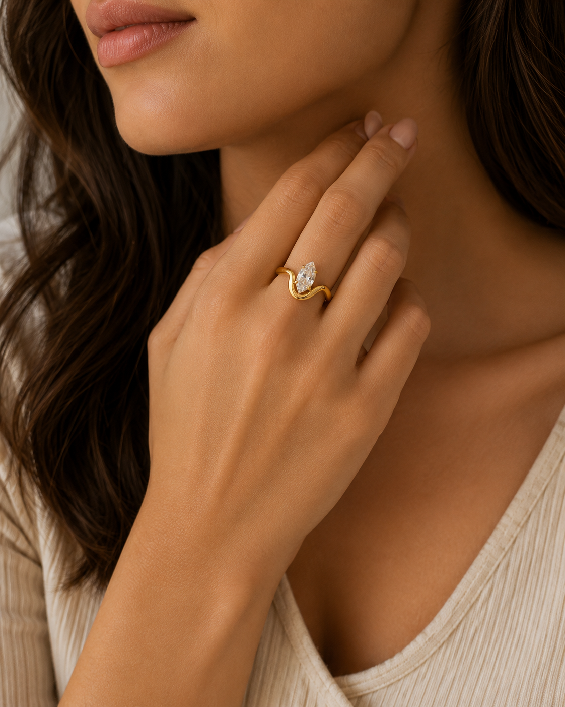 A close-up lifestyle shot of a woman wearing a gold ring with a marquise-cut clear gemstone on her finger. The ring features a textured, organic gold band with the stone set in the center.