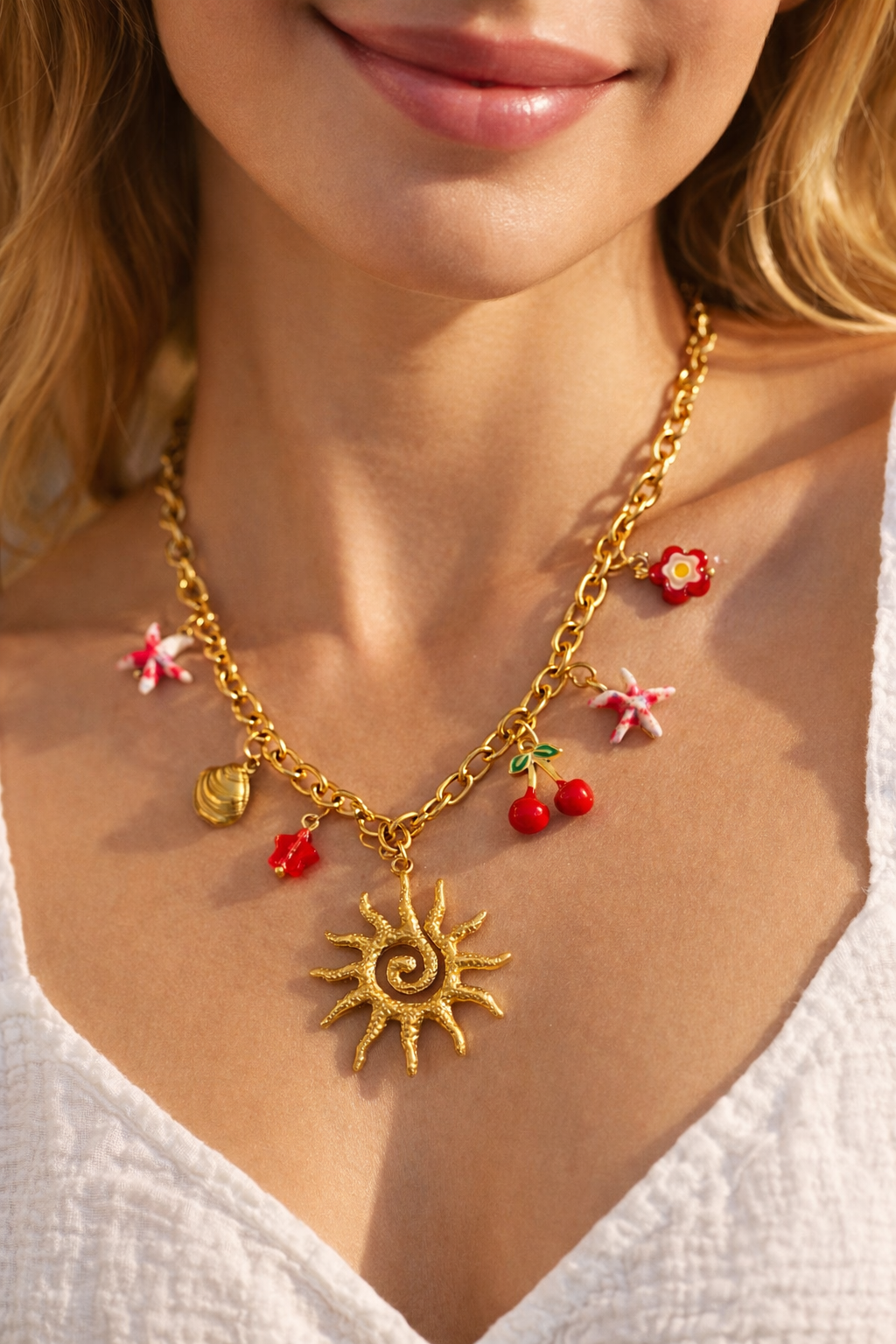 Gold necklace with sun pendant, red berries, and pink flowers worn by a person.