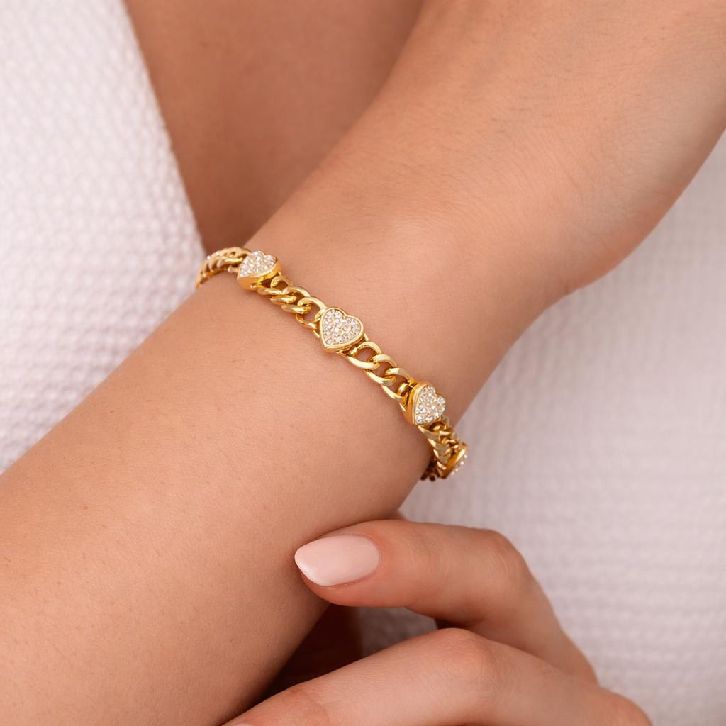 Gold chain bracelet with heart-shaped diamonds on a wrist against a light background