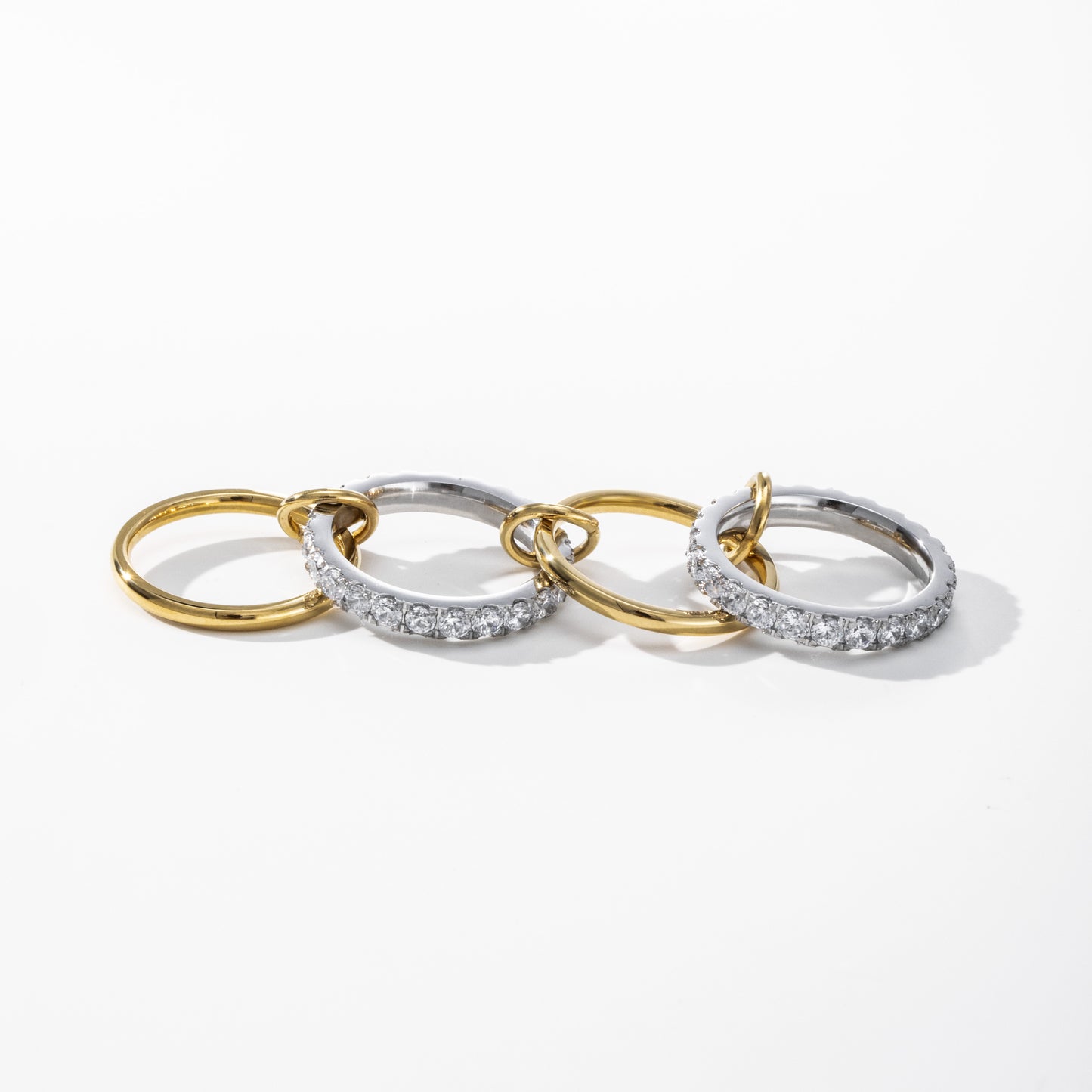 Three interlocking hoop earrings on a clean white background. Two hoops are yellow gold, and one is silver with a row of clear pavé stones.