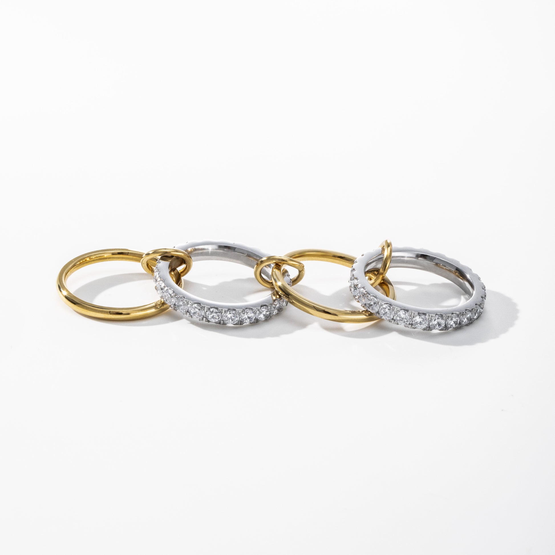 Three interlocking hoop earrings on a clean white background. Two hoops are yellow gold, and one is silver with a row of clear pavé stones.
