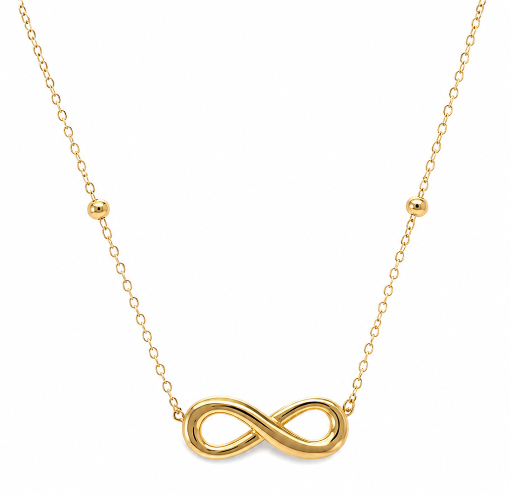 A gold necklace featuring a polished infinity symbol pendant at the center, suspended from a delicate gold chain with small gold bead accents on either side, set against a plain white background.