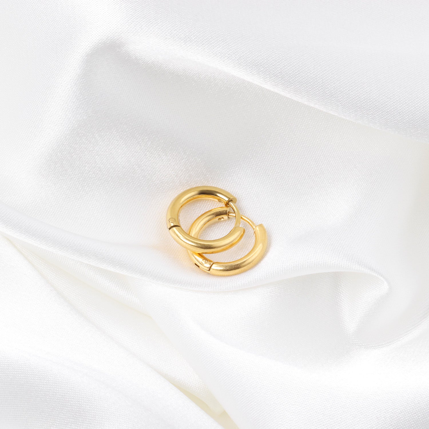 Gold hoop earrings on a white satin surface